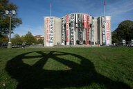 Das Gebäude der Volksbühne in Berlin ist mit Banern von Aufführungen verhüllt. Auf den Rasen vor der Volksbühne wirft das Räuberrad seinen Schatten auf die Wiese