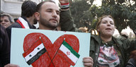 Ein Assad-Unterstützer hält ein Plakat mit einer syrischen, einer iranischen Flagge und einem Herz drumherum