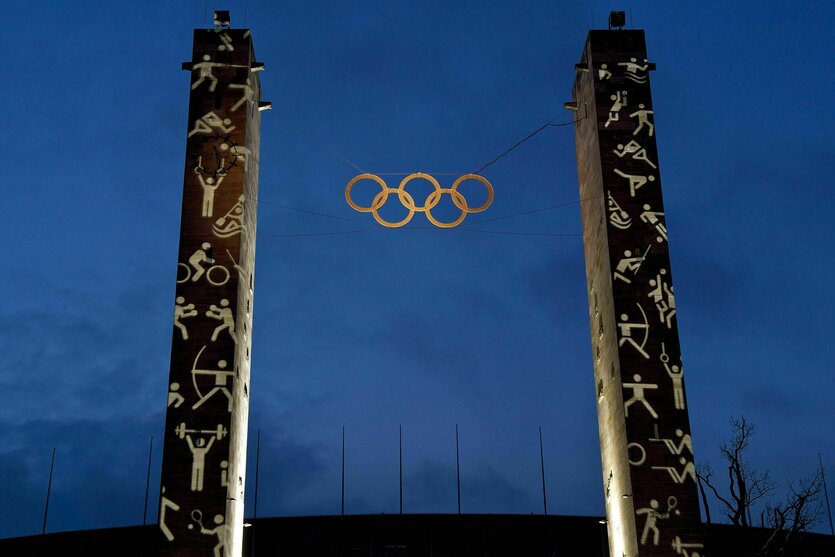 Das Marathontor des Berliner Olympiastadions wird mit Sport-Piktogrammen angestrahlt, zwischen den beiden Säulen hängen olympische Ringe