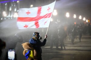 Das Bild zeigt eine Demonstrantin mit Gasmaske im Gesicht und einer georgischen Flagge in der Hand.