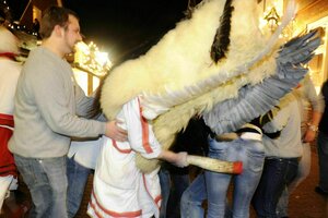 Ein Klaasohhm, ein verkleideter junger Mann der ein helles Gewand mit Fell aufdem Kopf und Kuhhorn in der Hand schlägt einer Frau auf den Hintern