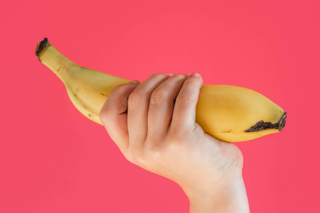 Kinderhand reckt eine Banan vor rosa Hhintergrund nach oben