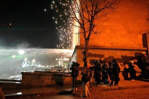 Journalisten gehen an der Ecke des Parlamentsgebäudes in Deckung. Auf der Straße sind Polizisten und Demonstrierende zu sehen, es ist Nacht