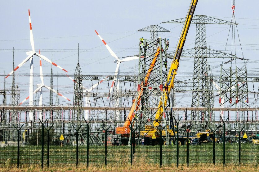 ARbeiten an Strommasten mit Kran, dahinter Windräder