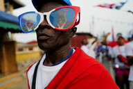 Ein Mann trägt eine riesige Sonnenbrille, in deren Gläsern sich der Regierungskandidat spiegelt.