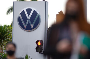 Großes VW-Logo, drumherum Menschen, unscharf