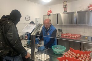 Kai Wegner in blauer Weste schenkt Kaffee an einen schwarzgekleideteten Mann in der Bahnhofsmission aus