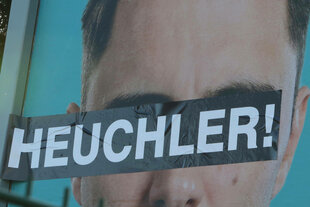 Auf einem Plakat sind die Augen eines Mannes überklebt mit dem Schriftzug "Heuchler"