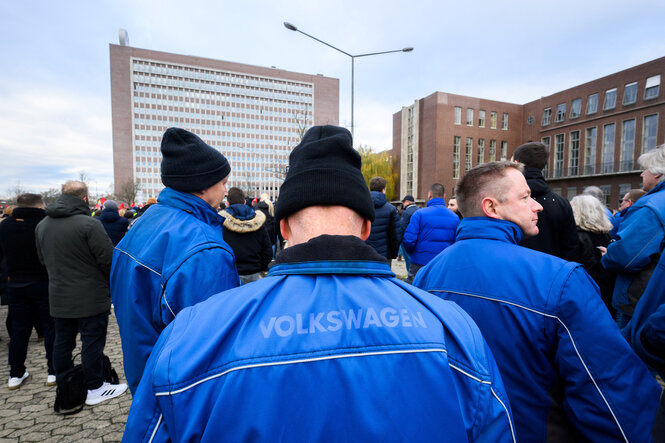 Menschen in blauer VW-Montur vor den Gebäuden eines Volkswagenwerks