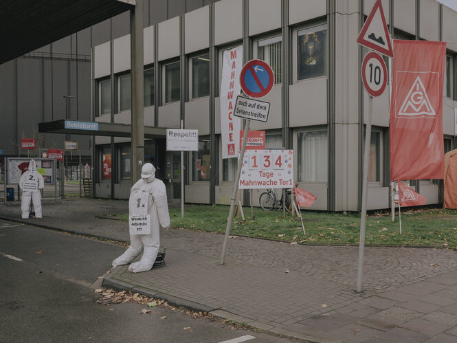 Weiße Gipsfiguren und Fahnen der IG Metall vor dem Eingang eines Fabrikgebäudes