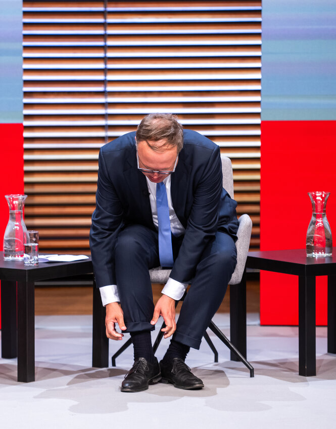 Mario Voigt sitzt auf einem Podium und krempelt sich die Hosenbeine hoch