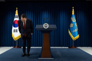 Der südkoreanische Präsident steht neben einem Stehpult und vor der südkoreanischen Fahne und verbeugt sich