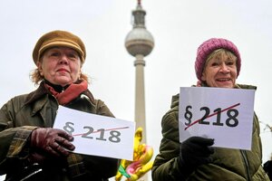 Zwei Frauen halten Schilder in die Höhe, auf denen 