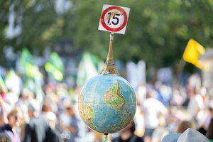 Einen Globus mit einem Miniatur-Eiffelturm und dem 1,5-Grad Ziel des Pariser Klimaschutzabkommens trägt ein Mann auf der Demonstration vor der Alten Oper in Frankfurt