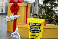 Eine Person hält ein Greenpeace-Plakat vor riesigen Geschenken. Darauf steht: "Milliardäre besteuern, Klima retten!"