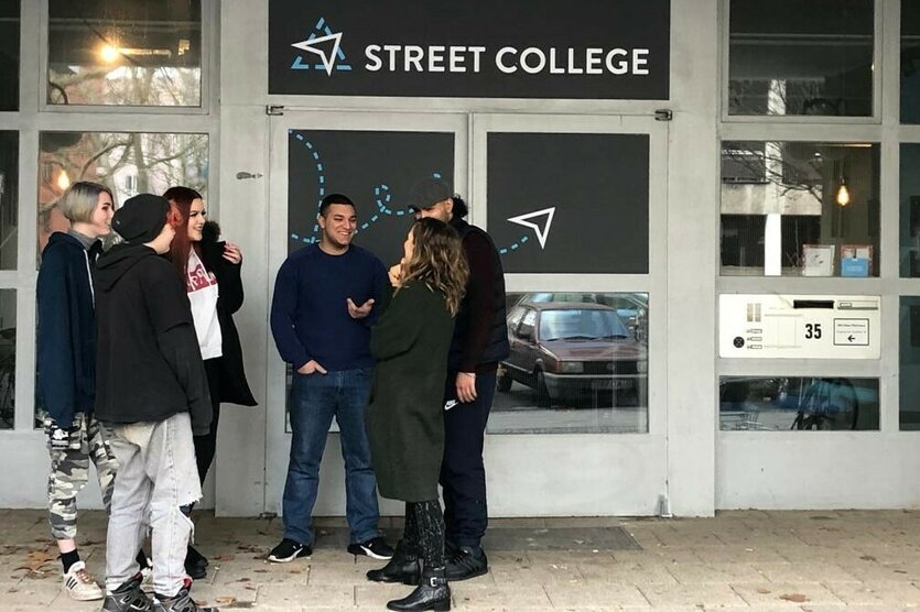 Jugendliche stehen draußen vor einer Tür mit der Aufschrift "Street College"