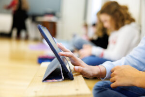 Schüler:innen in einem Klassenzimmer sitzen auf dem Boden und arbeiten an ihren Tablets