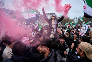 Menschen feiern ausgelassen mit den Fahnen der syrischen Opposition und roten Rauchfakeln