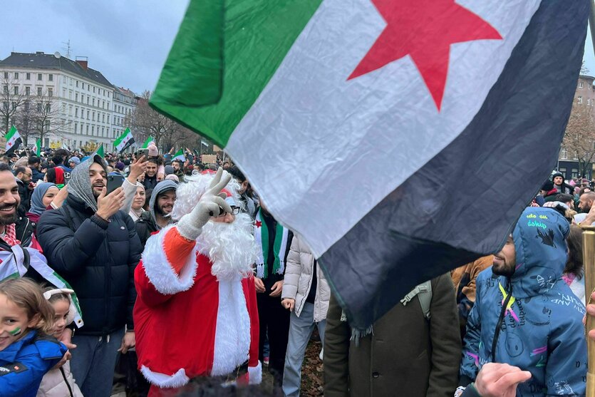 Eine als Weinachtsmann verkleidete Personin einer Menschenmenge mit Flaggen der syrischen Opposition