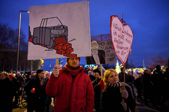 Bei einem Protest gegen Kürzungen im Kulturetat zeigen Demonstrierende ein Herz-Plakat, auf dem steht: "Klaus Lederer ich will eine Atelier/Förderung von Dir". Auf einem weiteren Plakat ist Kai Wegner als Auto abgebildet, der die freie Kunstszene, Fahrradwege und weitere Bausteine sozialer Politik frisst.