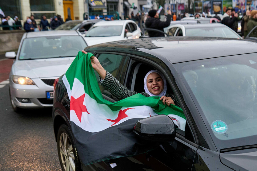 Eine Frau mit weißem Kopftuch schwänkt die Fahne der syrischen Rebellen aus einem schwarzen Auto heraus