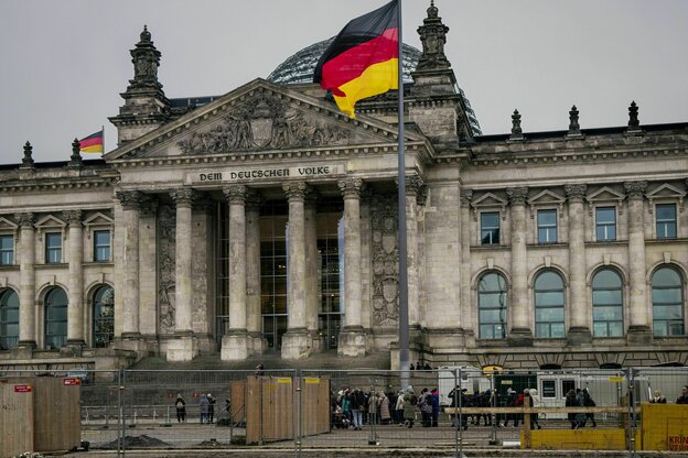 Das Reichstagsgebäude mit großer Deutschlandfahne, davor stehen Bauzäune und eine Besucherschlange