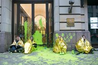 4 Aktivistinnen sitzen inmitten grüner Farbe vor einem Eingang des Adlon