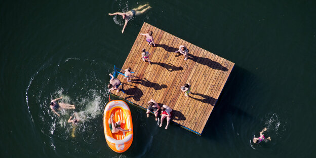 Aus der Luftperspektive sind Menschen auf einer Holzplattform in einem See zu sehen