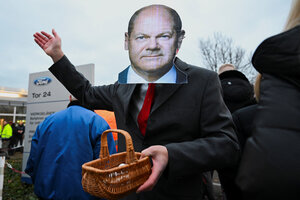 Ein Mann mit einer Gesichtsmaske von Olaf Scholz hält vor dem Parkplatz von Ford einen Korb in der Hand