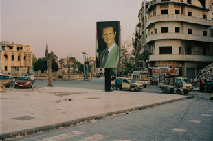 Übergroße Portraits von Bashar al-Assad hängen im leeren Stadtraum zwischen beschädigten Gebäuden