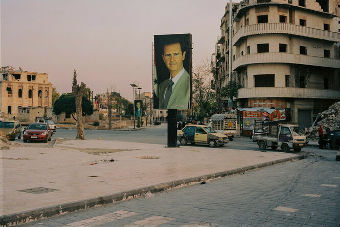 Übergroße Portraits von Bashar al-Assad hängen im leeren Stadtraum zwischen beschädigten Gebäuden