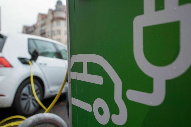 Ein Elektroauto lädt an einer Ladesäule in Halle Die Säule ist grün. Von dort fürt das Ladekabel in das Auto hinein. Das Auto ist weiß oder silbern.