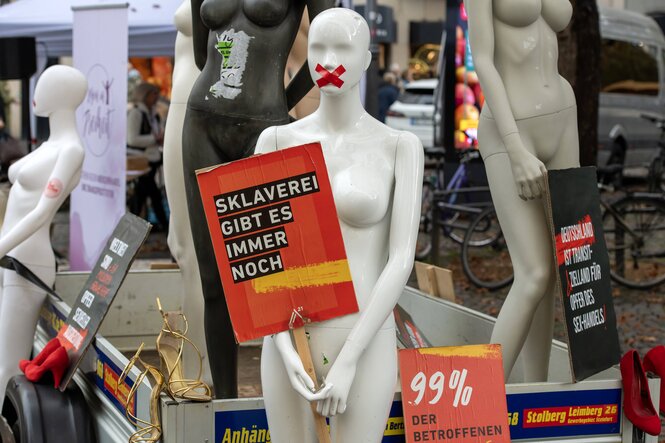 Eine weiße Schaufensterpuppe mit zugeklebtem Mund hält ein Schild mit der Aufschrift "Sklaberei gibt es immer noch"