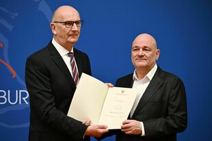 Dietmar Woidke und Robert Crumbach halten eine Urkunde in die Kamera