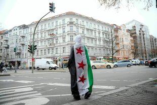 Eine in eine Fahne der syrischen Opposition gehüllte Person steht an einer Berliner Straßenkreuzung