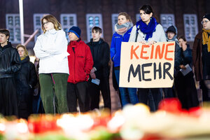 Menschen nehmen an einer Demonstration gegen Femizide in Hannover teil und stehen hinter niedergelegten Blumen und Kerzen - der Schriftzug 