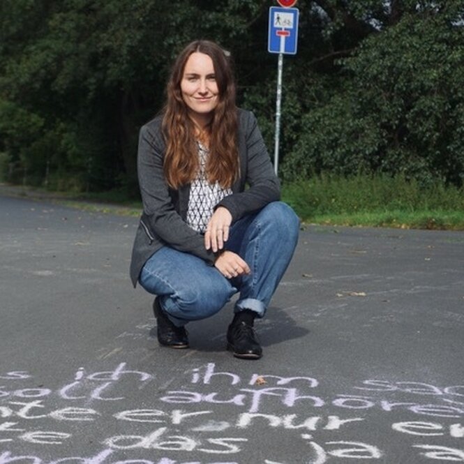 Eine Frau sitzt über einem Kreideschriftzug auf der Straße