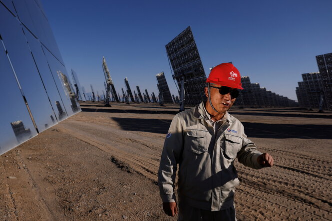 Ein chinesischer Arbeiter mit einem roten Bauhelm steht zwischen Solarpanelen