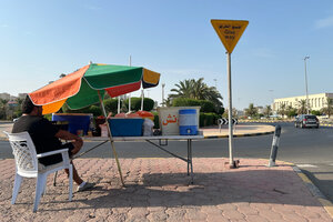 Ein Saatgutverkäufer in Kuwait sitzt bei sonnigem Wetter unter einem Sonnenschirm am Straßenrand