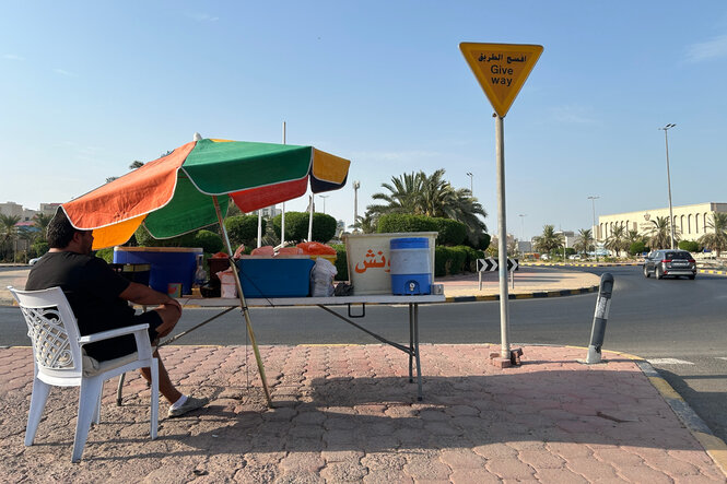 Ein Saatgutverkäufer in Kuwait sitzt bei sonnigem Wetter unter einem Sonnenschirm am Straßenrand