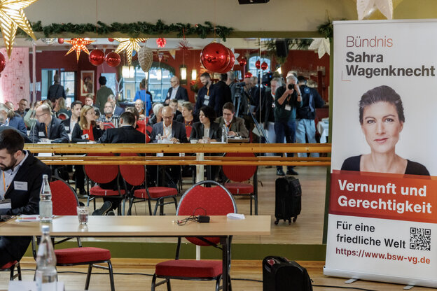 Menschen sitzen an Tischen in einem Raum mit Weihnachtsdekoration und einem Plakat, das Sahra Wagenknecht zeigt