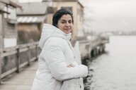 eine Frau in weißer Winterjacke lehnt an einem Gelände über einem See