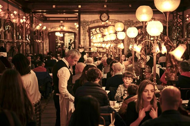 Ein gut gefüllter, prachtvoller Innenraum im Bouillon Chartier, in dem ein Kellner gerade Wein serviert.