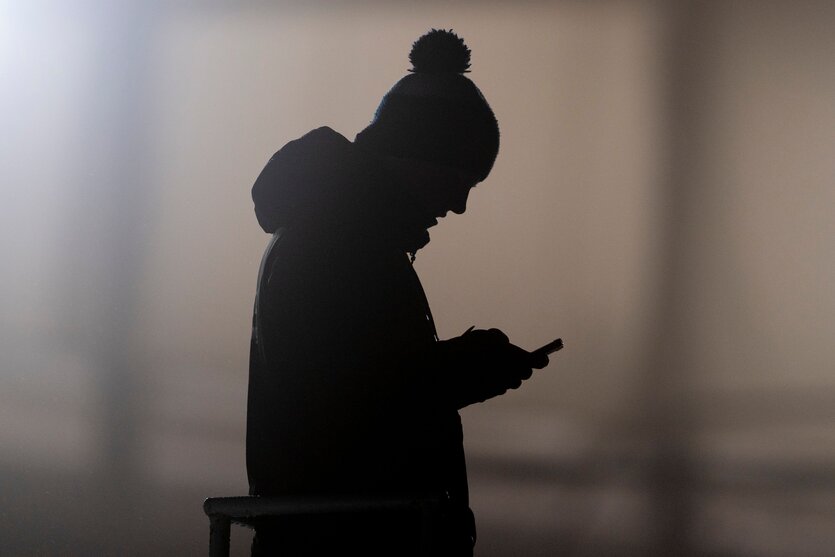 Die Silhouette eines Mannes ist zu sehen, der auf ein Smartphone schaut