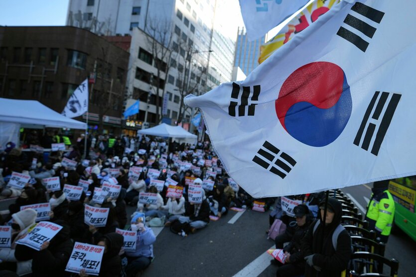 Menschen auf einer Demonstration halten Plakate in der Hand, im Vordergrund eine Flagge Südkoreas