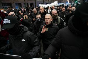 Schwarz gekleidete und glatzköpfige Demonstranten, einer zeigt das 