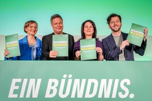 Die vier wichtigen Grünen, zwei Frauen, zwei Männer stehen mit der Broschüre "Zusammen wachsen" lächelnd auf dem Podium. Vor ihnen der Schriftzug Bündnis