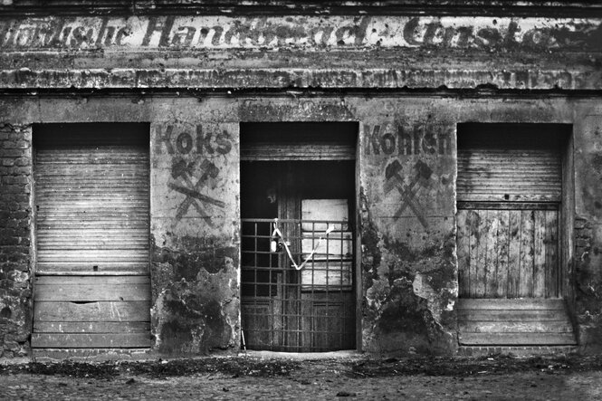 Die Fassade eines alten Ladens für Koks und Kohlen, alte Wandschriften, mürbes Mauerwerk, Türen verbarrikadiert