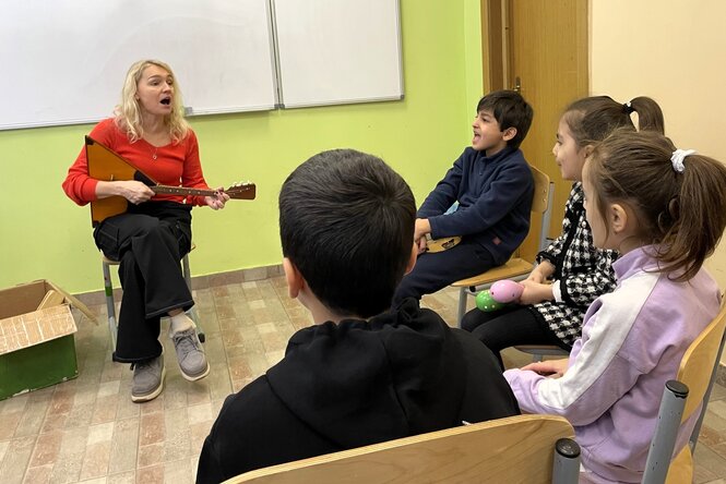 Eine Frau spielt Gitarre, mehrere Schüler sitzen im Stuhlkreis um sie herum