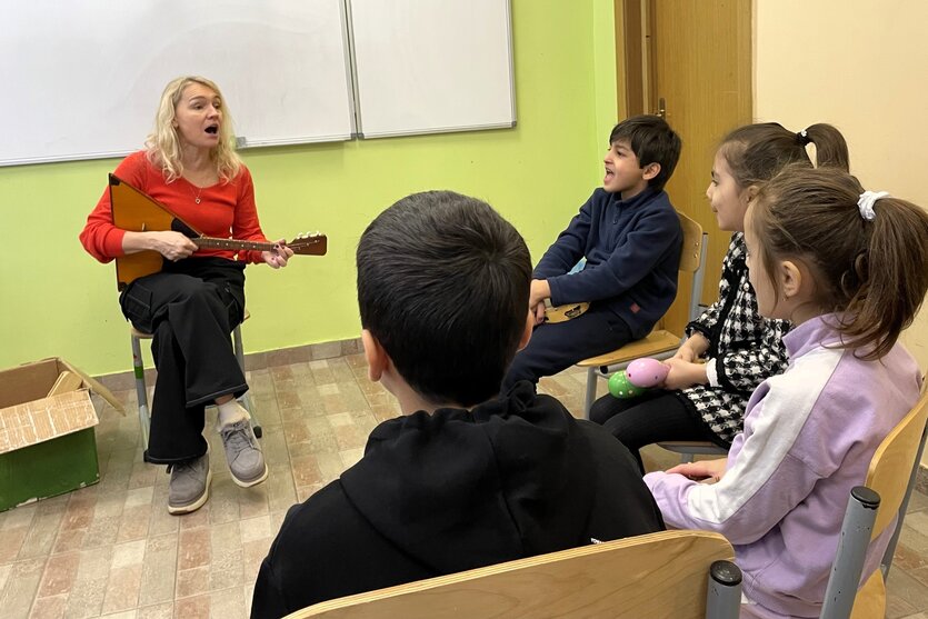 Eine Frau spielt Gitarre, mehrere Schüler sitzen im Stuhlkreis um sie herum